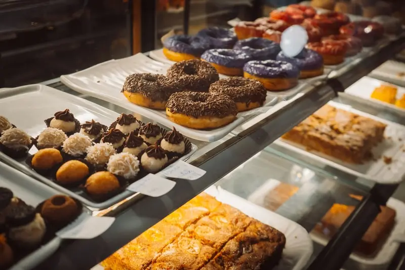 A bakery counter display of doughnuts, iced buns and pastries behind glass.